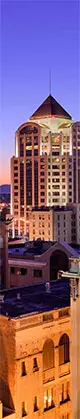 Roaonke Virginia city skyline at dusk featuring a prominent large building in the foreground, with colorful lights illuminating the scene.