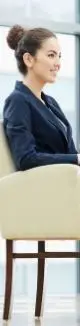 A woman in a business suit sits confidently on a chair, exuding professionalism and poise in a corporate setting.