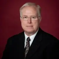 headshot of man in black suit with red background