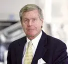 headshot of man standing in car dealership wearing a black suit with yellow tie
