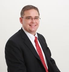 headshot of many in black suit with red tie